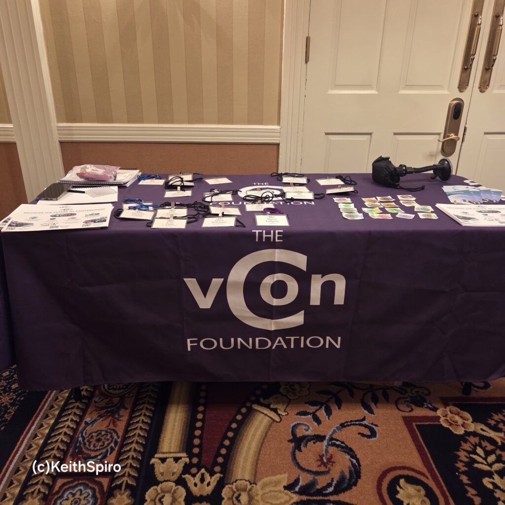 a photo by Keith Spiro depicting the welcome table banner for the vCons conference.